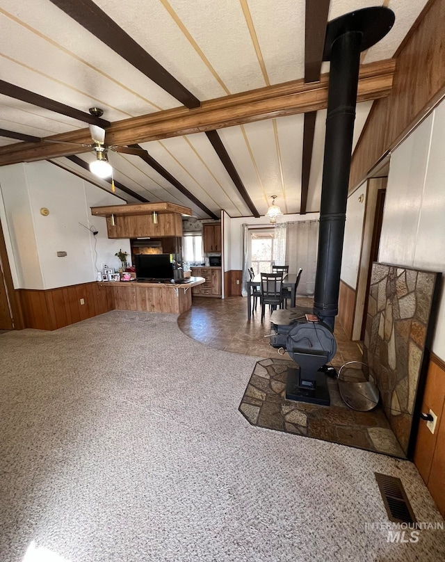 living room with carpet flooring, vaulted ceiling with beams, a wood stove, and ceiling fan