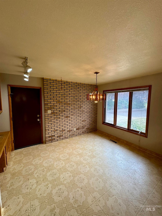 unfurnished room with a notable chandelier, a textured ceiling, and brick wall