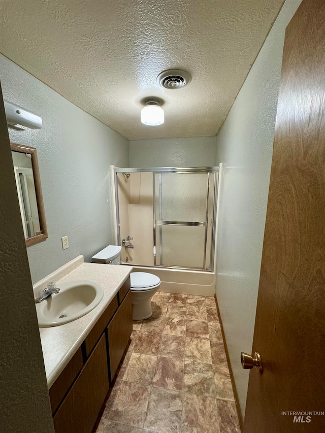 full bathroom featuring a textured ceiling, vanity, toilet, and shower / bath combination with glass door