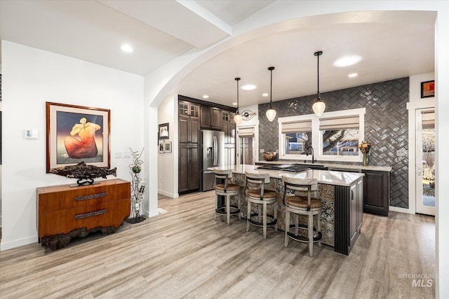 kitchen featuring decorative light fixtures, a kitchen island, stainless steel refrigerator with ice dispenser, a kitchen bar, and light stone countertops