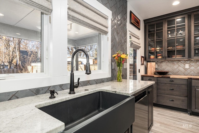 kitchen with light hardwood / wood-style floors, dishwasher, light stone countertops, dark brown cabinetry, and sink