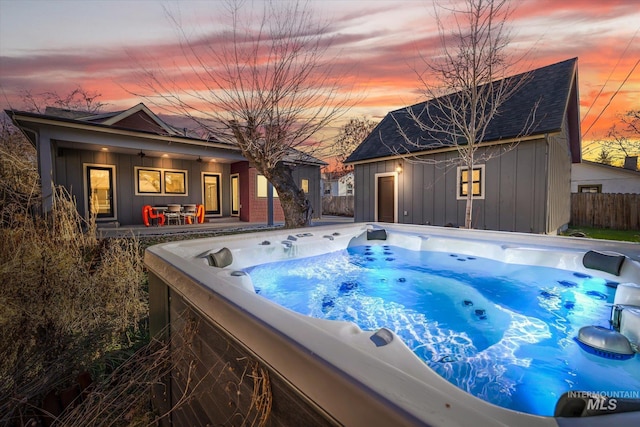 pool at dusk featuring an outbuilding and a hot tub