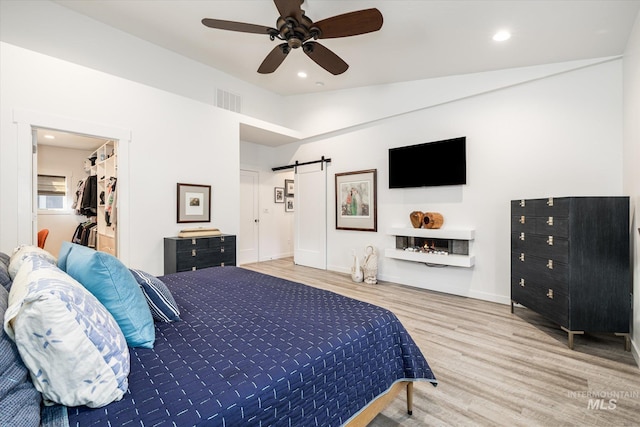 bedroom featuring a spacious closet, lofted ceiling, hardwood / wood-style flooring, ceiling fan, and a barn door