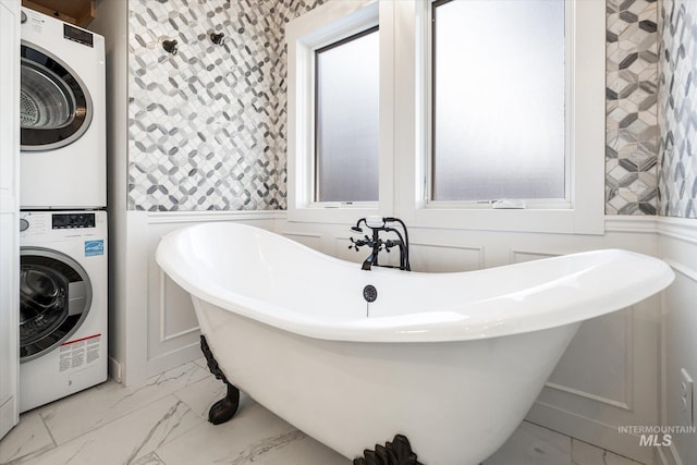 bathroom featuring stacked washing maching and dryer and a tub