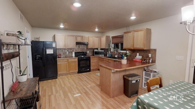 kitchen featuring kitchen peninsula, light brown cabinets, a breakfast bar, and black appliances