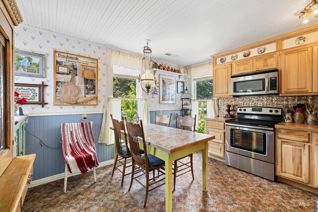 kitchen with appliances with stainless steel finishes, pendant lighting, light brown cabinetry, and wooden walls