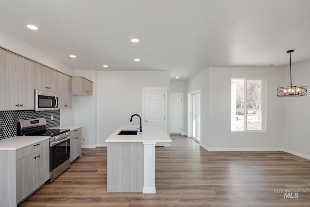 kitchen featuring sink, hardwood / wood-style floors, an island with sink, decorative light fixtures, and appliances with stainless steel finishes