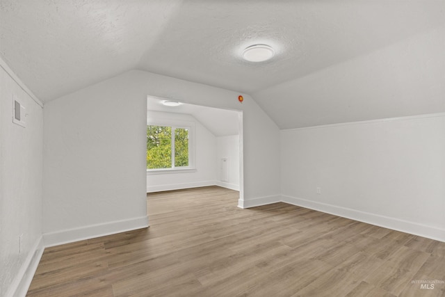 additional living space with lofted ceiling, wood-type flooring, and a textured ceiling