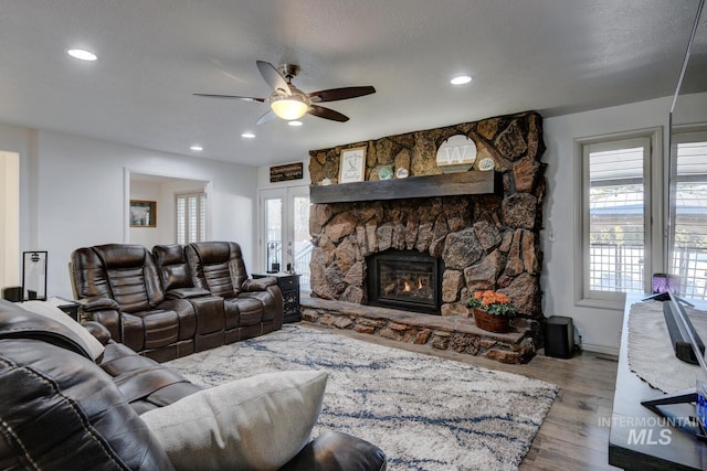 living room featuring hardwood / wood-style flooring, ceiling fan, a stone fireplace, and a textured ceiling