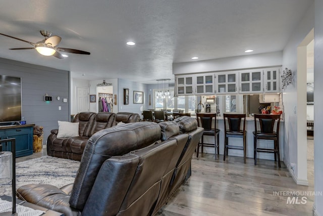 living room featuring ceiling fan with notable chandelier, a textured ceiling, and light wood-type flooring