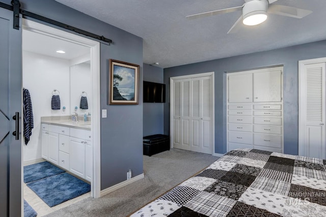 bedroom featuring light carpet, two closets, a barn door, and ceiling fan