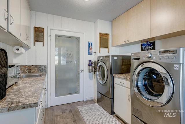 clothes washing area with cabinets, light wood-type flooring, a textured ceiling, and independent washer and dryer