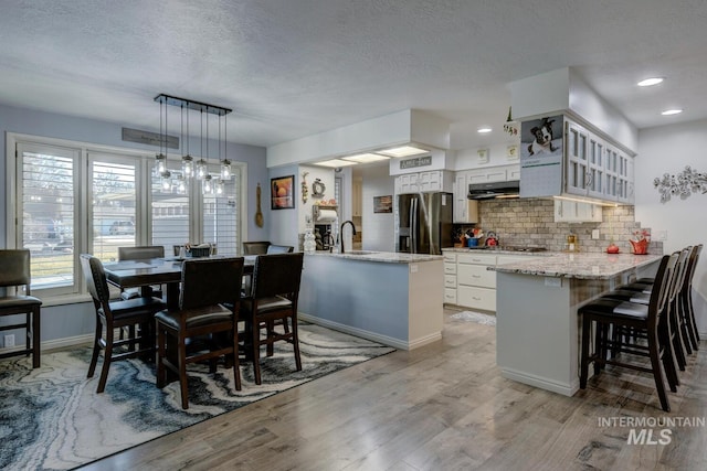 kitchen with a kitchen bar, white cabinetry, decorative light fixtures, stainless steel fridge, and kitchen peninsula