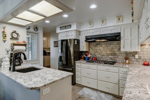 kitchen featuring sink, appliances with stainless steel finishes, white cabinetry, light stone countertops, and kitchen peninsula