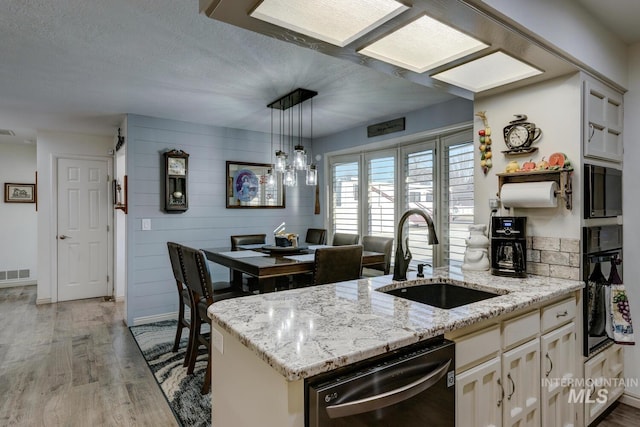 kitchen featuring sink, light hardwood / wood-style flooring, hanging light fixtures, black appliances, and wood walls