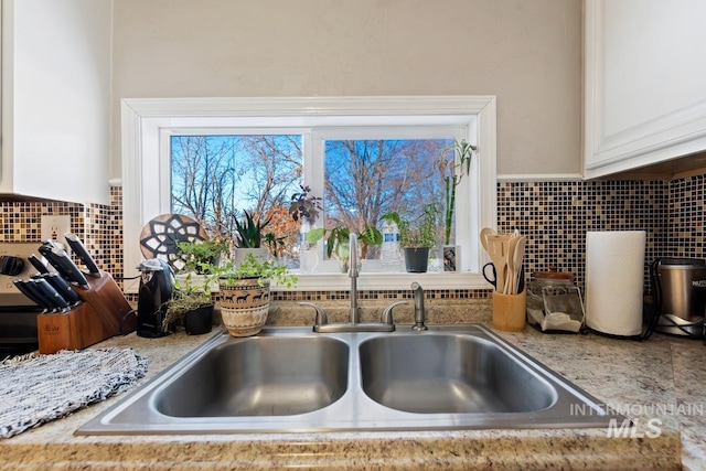 interior details featuring sink, light stone counters, white cabinets, and backsplash