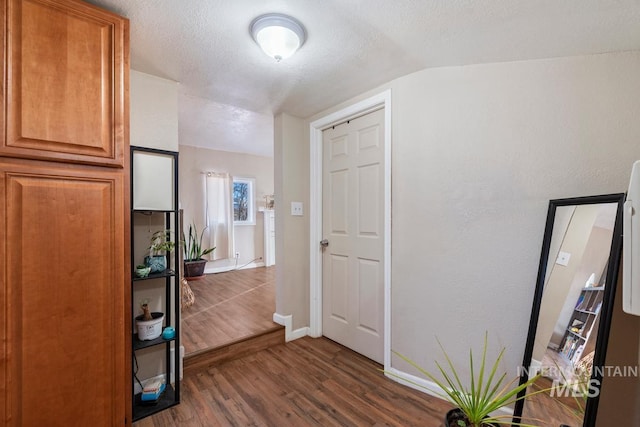 hall featuring dark hardwood / wood-style flooring, vaulted ceiling, and a textured ceiling