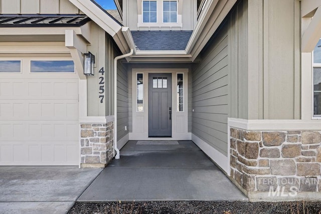 entrance to property featuring a garage, stone siding, and roof with shingles