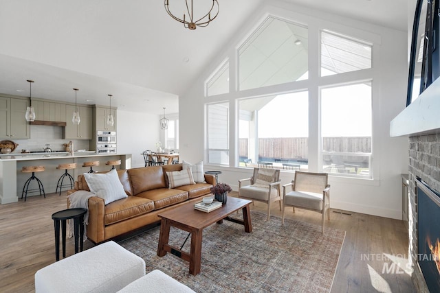 living room featuring a brick fireplace, high vaulted ceiling, an inviting chandelier, and light wood-type flooring