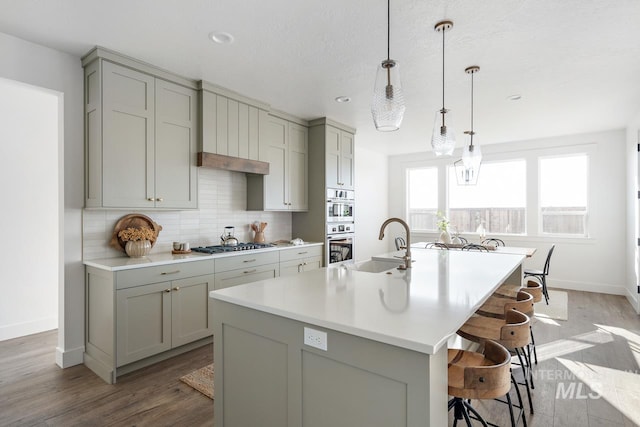 kitchen with a sink, light countertops, gray cabinets, tasteful backsplash, and a center island with sink