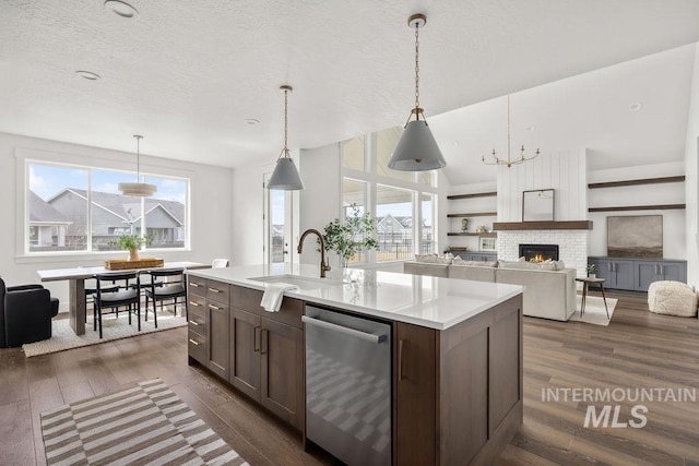 kitchen featuring dark wood finished floors, light countertops, stainless steel dishwasher, a kitchen island with sink, and a sink