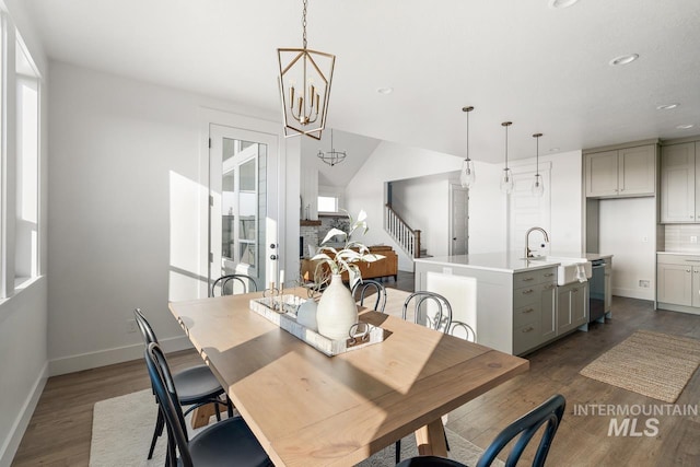 dining space featuring a stone fireplace, sink, an inviting chandelier, dark hardwood / wood-style flooring, and vaulted ceiling