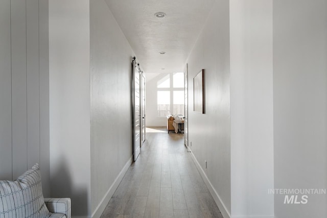 corridor with wood finished floors, baseboards, and a barn door