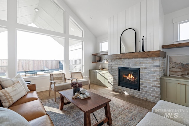 living room with high vaulted ceiling, a brick fireplace, and wood finished floors