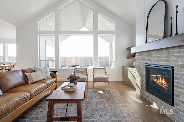 living room featuring vaulted ceiling, a brick fireplace, wood finished floors, and baseboards