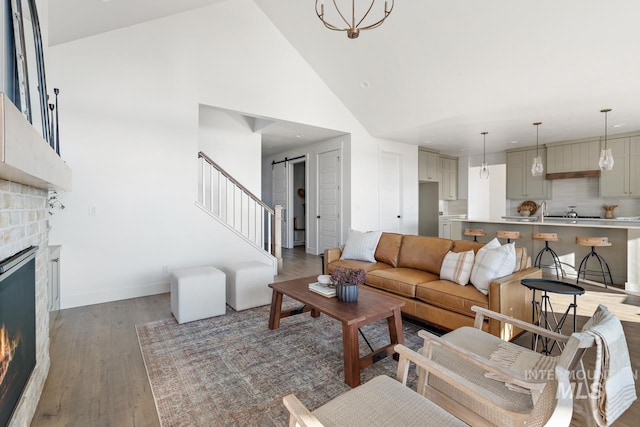 living area with a barn door, baseboards, dark wood-style flooring, a stone fireplace, and high vaulted ceiling