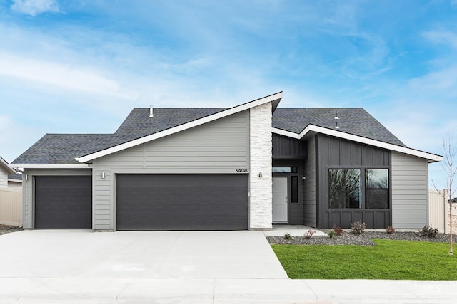 mid-century home with a garage, a shingled roof, board and batten siding, and concrete driveway