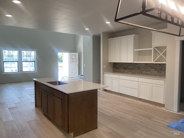 1640 E Cutgrass Ln, Eagle, ID 83616 - kitchen featuring backsplash, a center island with sink, light wood-style flooring, white cabinetry, and light countertops