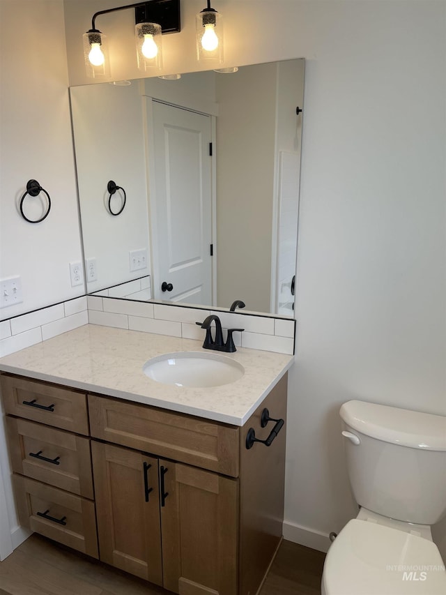 bathroom with toilet, vanity, baseboards, and wood finished floors