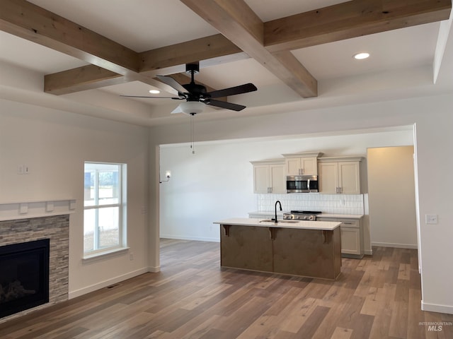 kitchen featuring a sink, stainless steel microwave, a fireplace, decorative backsplash, and baseboards