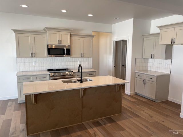 kitchen with a sink, stainless steel appliances, wood finished floors, and a center island with sink