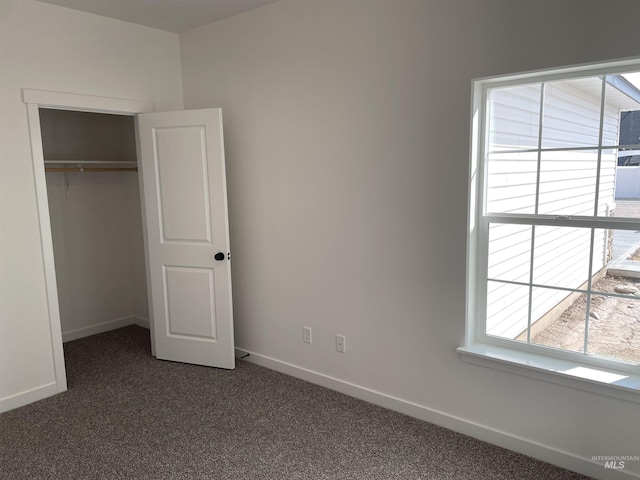 unfurnished bedroom featuring dark colored carpet, a closet, and baseboards