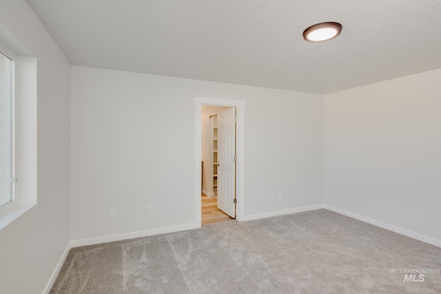 spare room with a textured ceiling, carpet, and baseboards