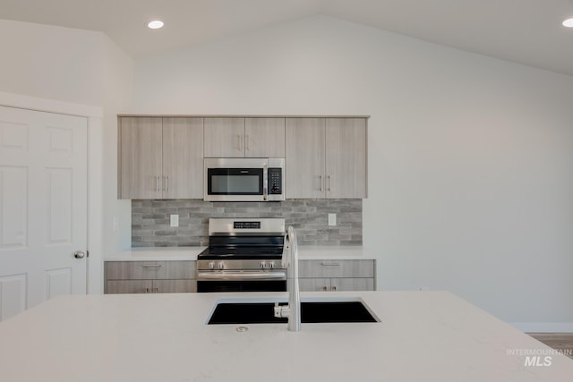 kitchen featuring vaulted ceiling, light countertops, appliances with stainless steel finishes, light brown cabinetry, and modern cabinets