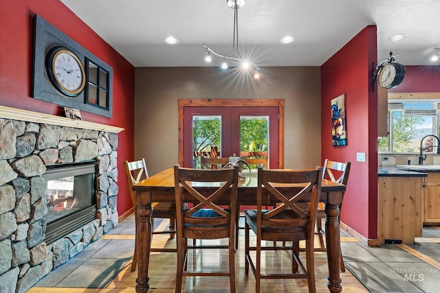 dining room with light wood-type flooring, sink, a notable chandelier, and a stone fireplace