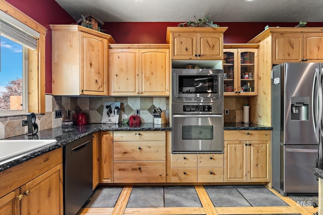 kitchen with dark stone counters, backsplash, stainless steel appliances, sink, and light brown cabinets