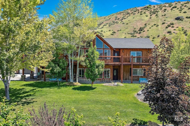 back of property with a balcony, a mountain view, and a lawn