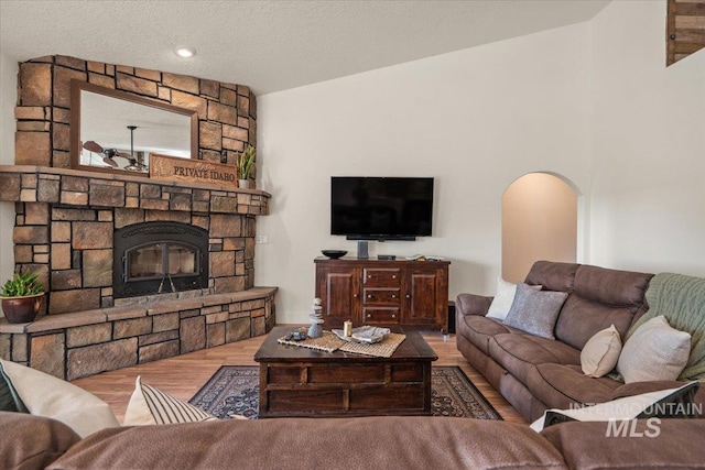 living room featuring arched walkways, a fireplace, vaulted ceiling, and wood finished floors