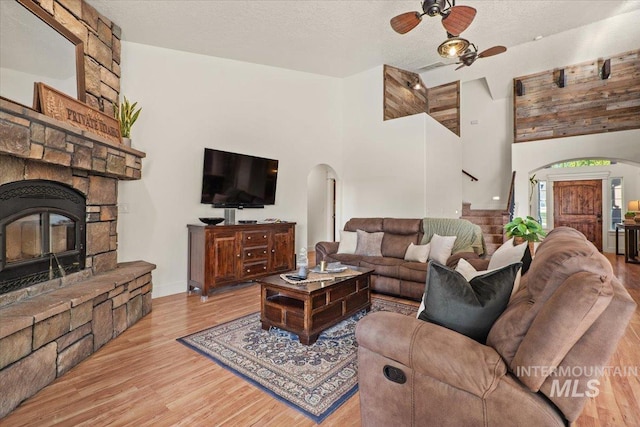living room with arched walkways, a textured ceiling, a ceiling fan, wood finished floors, and a towering ceiling