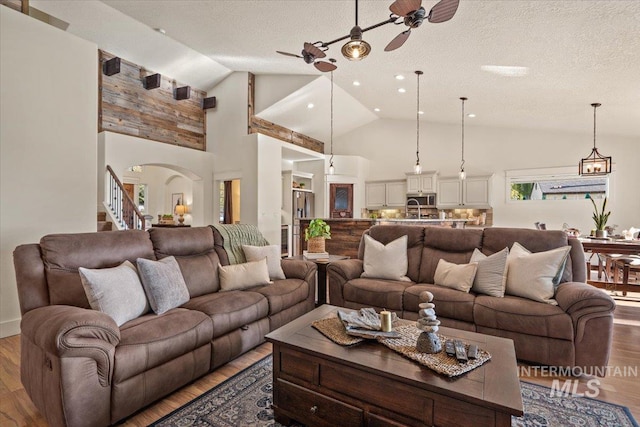 living room with arched walkways, a ceiling fan, light wood-type flooring, and a textured ceiling