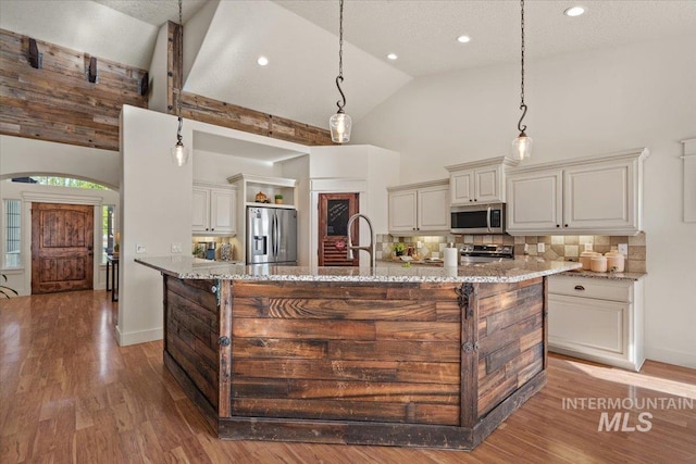 kitchen with appliances with stainless steel finishes, light stone counters, light wood finished floors, high vaulted ceiling, and tasteful backsplash