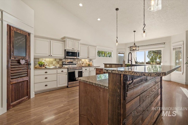 kitchen with light wood-style flooring, dark stone counters, stainless steel appliances, tasteful backsplash, and a spacious island