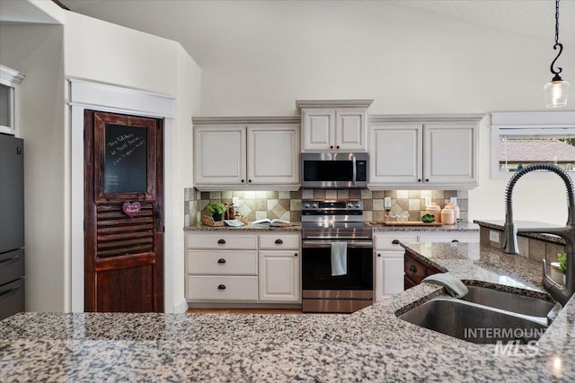 kitchen with light stone countertops, a sink, appliances with stainless steel finishes, backsplash, and hanging light fixtures