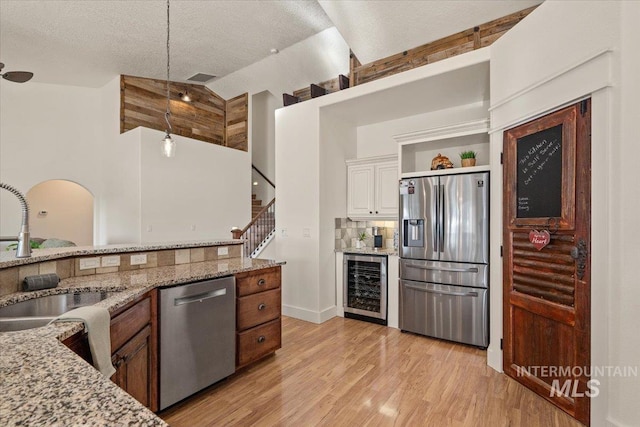 kitchen with pendant lighting, wine cooler, a sink, light wood finished floors, and stainless steel appliances