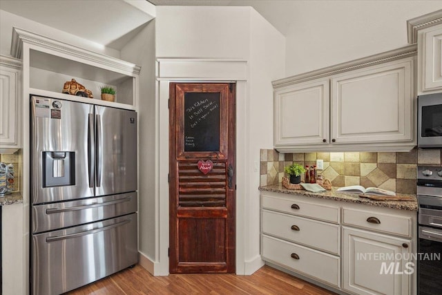 kitchen with backsplash, light stone countertops, light wood-type flooring, baseboards, and stainless steel appliances