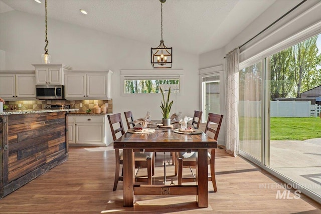 dining area with a chandelier, a wealth of natural light, light wood finished floors, and lofted ceiling